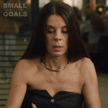 a woman in a black strapless dress with the words small achievable goals on the bottom right