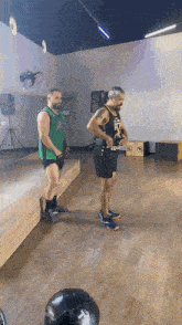 two men are standing in a gym with one wearing a green jersey that says jc