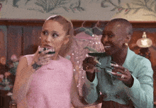 a woman in a pink dress holds a glass of wine next to a woman in a green jacket