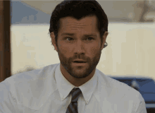 a man with a beard wearing a white shirt and tie looks at the camera