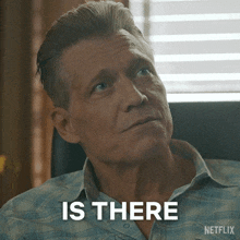 a man in a plaid shirt is sitting in front of a window and says " is there "
