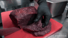 a person is cutting a large piece of meat on a red cutting board that says made in animatica