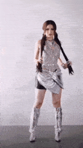 a woman is standing in a room wearing a silver dress and boots .
