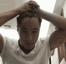 a man in a white t-shirt is holding his hair in a bun