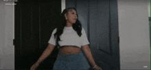 a woman is standing in front of a door wearing a white crop top and blue shorts .