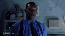 a man in a blue shirt and tie is making a funny face in a dark room .