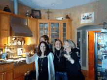 three women are posing for a picture in a kitchen with a picture of a cross on the wall
