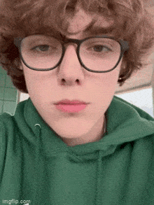 the boy is wearing glasses and a green hoodie .