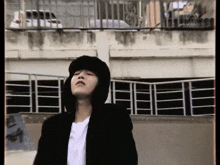 a young man wearing a hooded jacket and a hat stands in front of a building .
