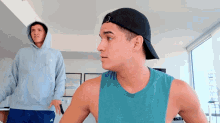 a man wearing a hat and a hoodie stands next to another man
