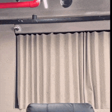 a couch sits in front of a window with white curtains and a red pipe hanging from the ceiling