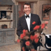 a man in a tuxedo and bow tie is holding a vase of flowers .