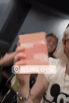 a person in a beijing china shirt is holding a pink box