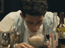 a man sitting at a table eating a dessert with a bottle of wine in the background