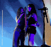a woman singing into a microphone next to another woman holding a guitar