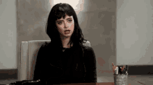 a woman is sitting at a desk with a pencil holder and making a funny face .