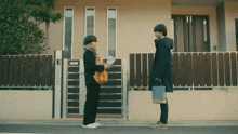 a man standing next to a woman holding a bag and a piece of paper in front of a house