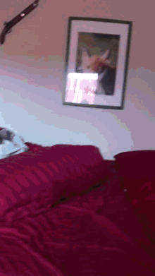 a bed with red sheets and a framed picture on the wall above it