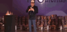 a man is standing on a stage holding a microphone in front of a stack of books