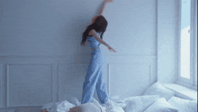 a woman in blue pants and a blue top is standing on a bed