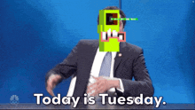 a man in a suit and tie is sitting at a desk and says today is tuesday