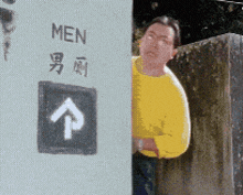 a man in a yellow shirt stands in front of a sign that says men on it