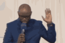a man in a blue suit is holding a microphone and waving his hand in the air .