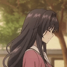 a girl with long black hair is standing in front of a tree and looking down .