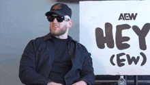 a man wearing sunglasses sits in front of a sign that says hey