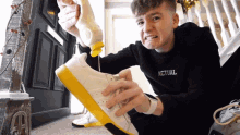 a boy wearing a black sweater that says actual is cleaning his shoes