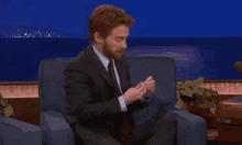 a man in a suit and tie is sitting in a chair with his legs crossed