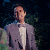 a man wearing a purple suit and a pink bow tie is laughing