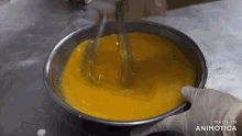 a person is mixing a yellow liquid in a metal bowl with the words made in animotica on the bottom