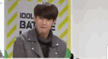a man in a gray jacket is standing in front of a sign that says `` idol battle '' .