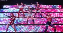 a group of women are standing on top of a stage in front of a colorful background .