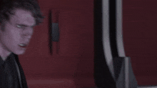 a man in a black suit is standing in front of a red wall
