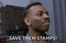 a man is smiling and saying `` save them stamps '' while standing in front of a building .