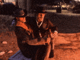 two men in cowboy hats are sitting on a bench holding beer bottles