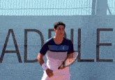 a man is holding a tennis racquet in front of a sign that says adelle