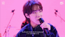 a young man is singing into a microphone in a pink room