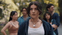 a woman wearing a necklace stands in front of a crowd of people