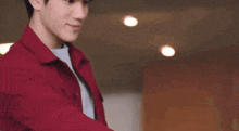 a young man in a red shirt is standing in a room and smiling at the camera .