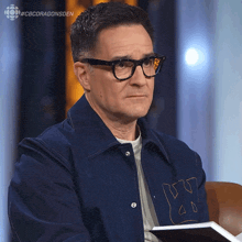 a man wearing glasses and a blue jacket with the letter x on the back