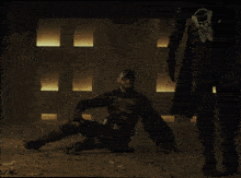 a man is kneeling down while a woman stands behind him in a dark room