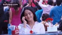 a woman is sitting at a table in a crowded restaurant talking on a cell phone .