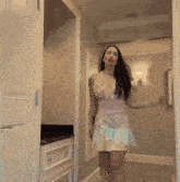 a woman in a pink and white dress stands in a hallway