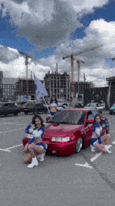 a group of cheerleaders posing in front of a red car
