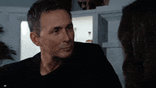 a man in a black suit looks at a woman in a black t-shirt