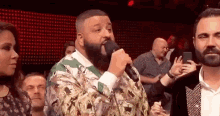 a man with a beard is singing into a microphone while standing in front of a crowd .