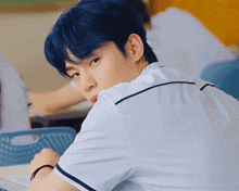 a young man with blue hair is sitting in a classroom